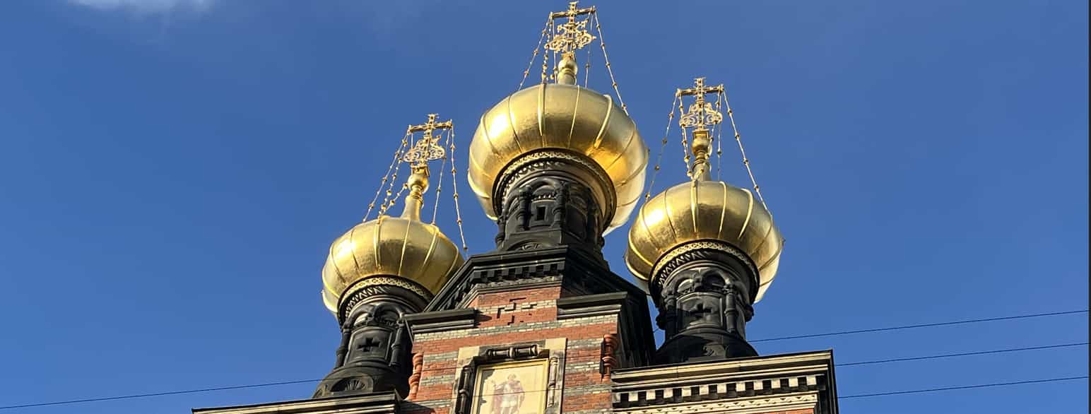 Tre kupler i gull på en bygning av murstein. På toppen av kuplene er det kors.
