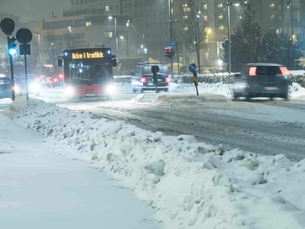 Gater som er fulle av snø, og det snør tett. På bildet er det noen biler og en buss hvor det står "ikke i trafikk" på.