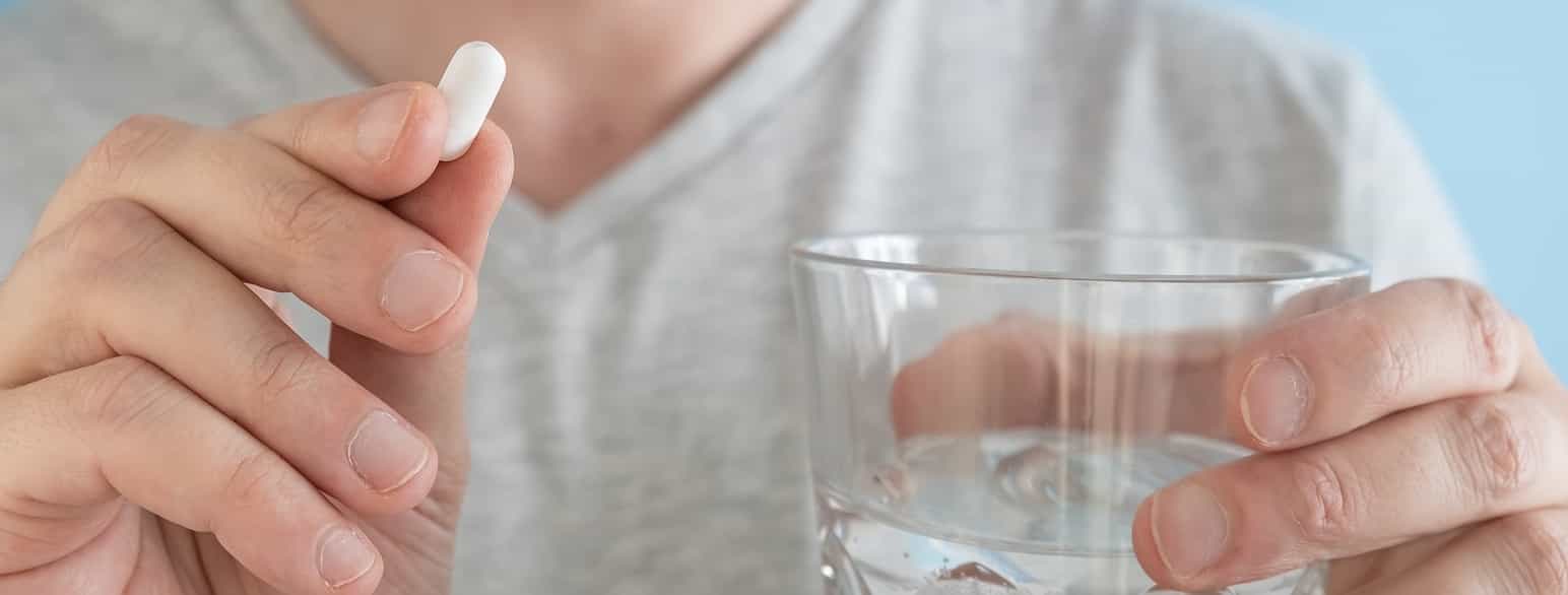 Mann holder en pille og et glass med vann