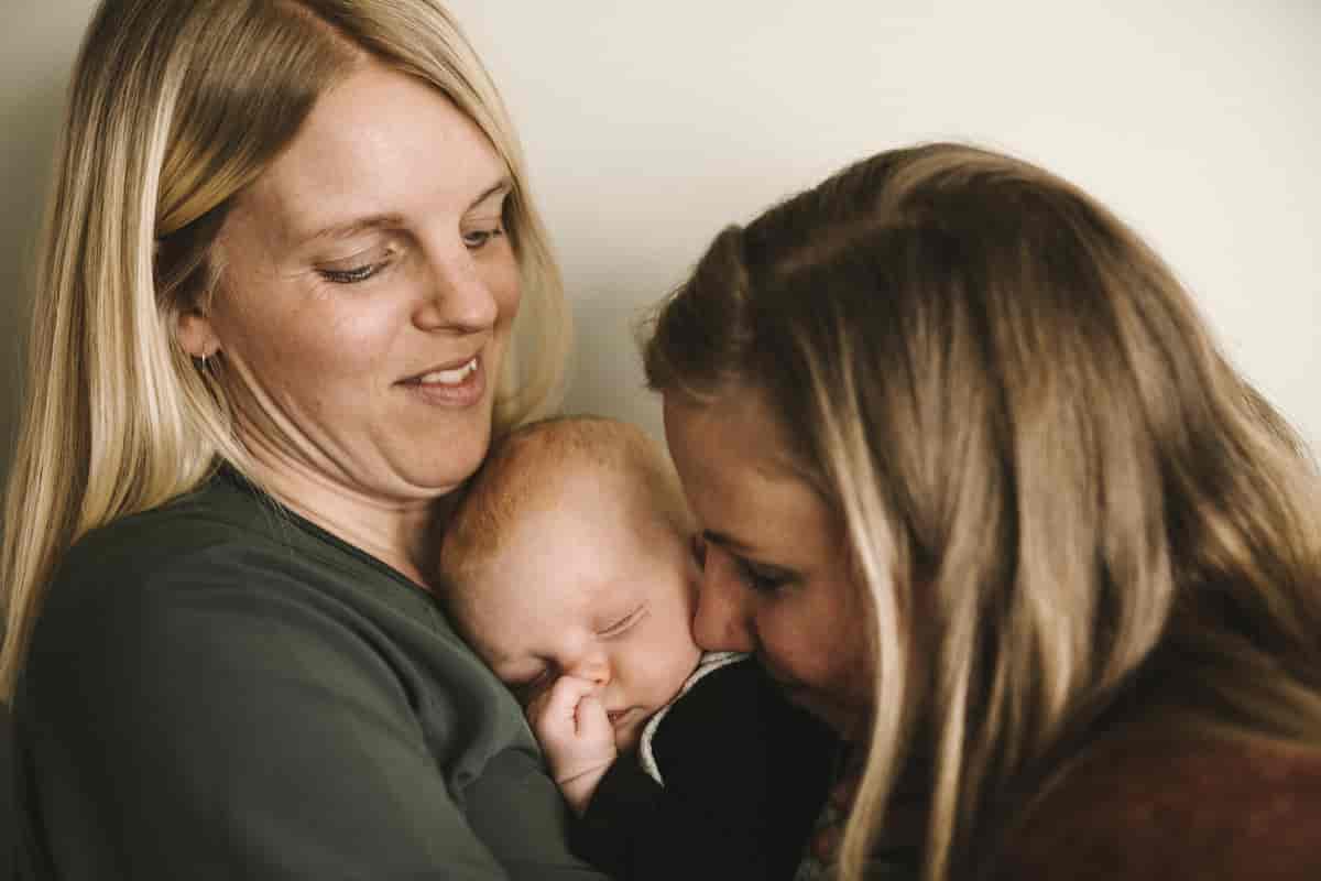 To kvinner held rundt kvarandre og ein baby. 
