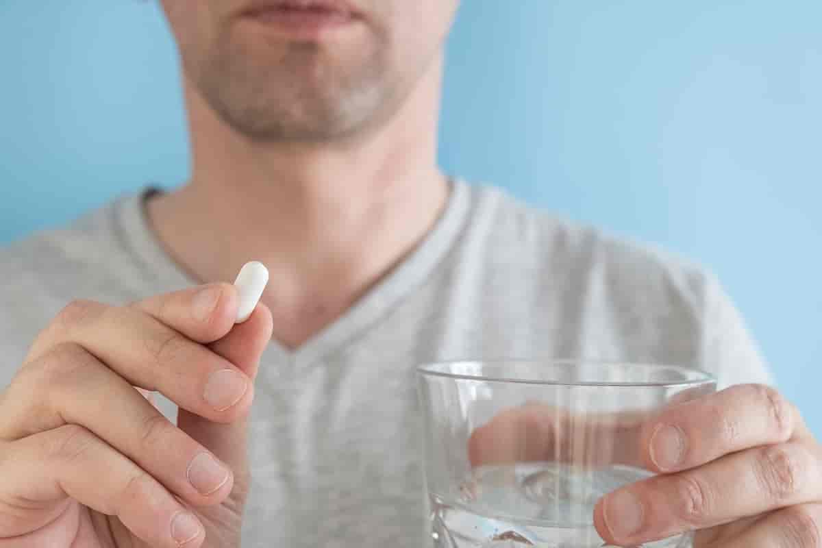 Foto av mann som holder vannglass og hvit tablett