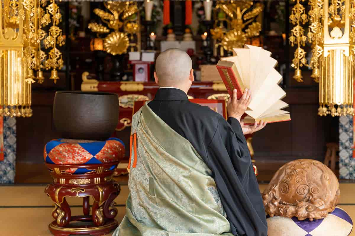 En mann sitter med ryggen til og holder i en bok med oppslåtte sider. han sitter på gulvet foran et alter som er pyntet i gull og rødt
