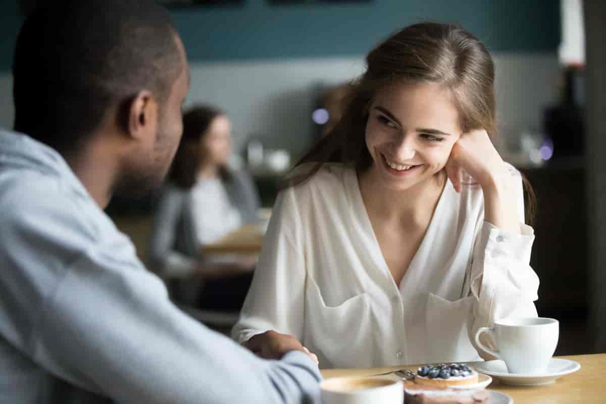 Kvinne smiler til en mann over et cafebord ut. Hun ser ham i øynene. 