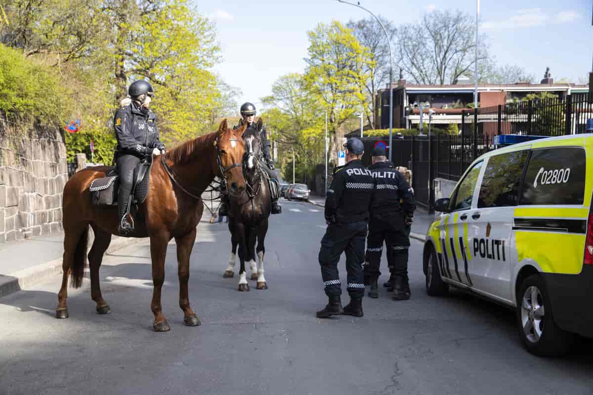 To politikvinner på hver sin hest, og to politimenn utenfor en politibil