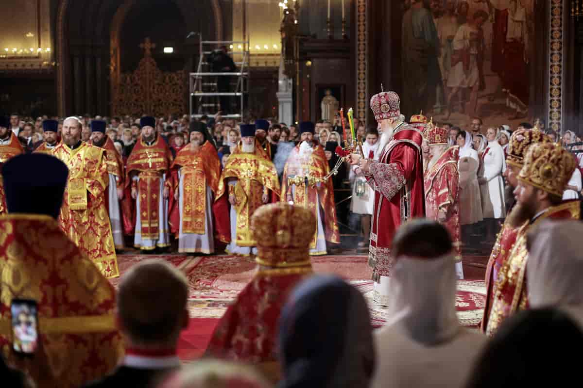Bildet viser innsiden av en kirke. Mennene på bildet er pyntet med religiøse klær i rødt og gull. I midten er patriarken. han holder tre lys i grønt, gult og rødt. På hodet har han en rund hatt i rødt og sølv.