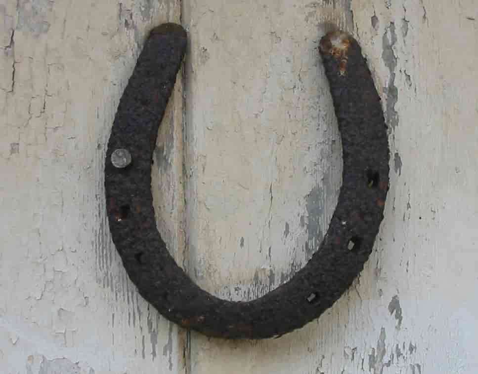 Foto av en gammel, rusten  hestesko henger på en hvitmalt vegg med buen ned.