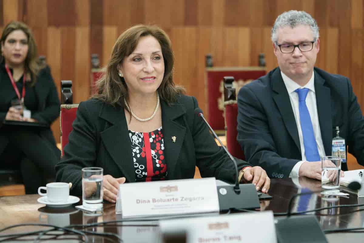 Fotografi av Boluarte som sitter ved et bord med mikrofon foran seg. Ved siden av henne sitter generaldirektør i VIPO (Den internasjonale opphavsrettsorganisasjonen). I bakgrunnen sitter en journalist.