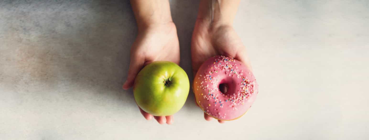 Bildet viser et eple i én hånd og en donut i den andre. 