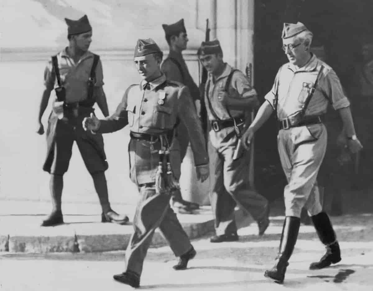 Gammelt sort-hvitt fotografi av Franco, som marsjerer i uniform med to andre menn etter seg. Ytterligere to menn i bakgrunnen ser ut til å holde vakt utenfor en bygning.