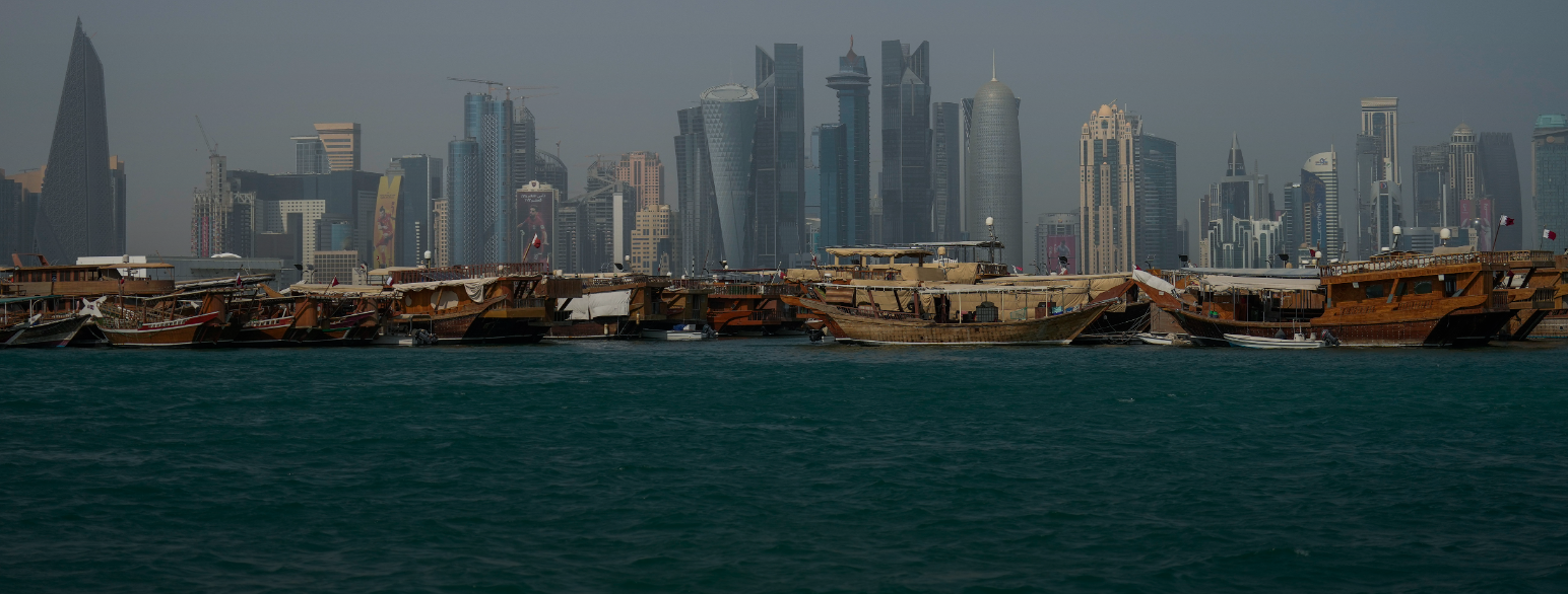 Tradisjonelle trebåter ligger til ankers i havnen i Doha med den moderne byen med skyskrapere i bakgrunnen. 