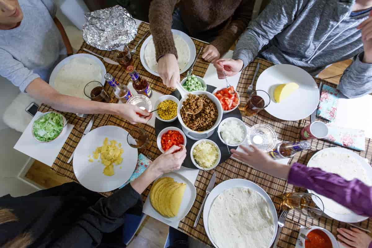 Foto tatt ovenfra, hvor det er servert norsk taco på et stort bord. Flere personer sitter til bords, og forsyner seg av maten. 
