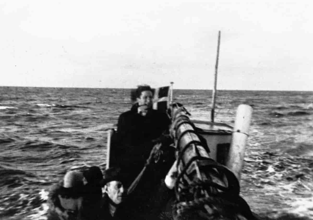 Sort-hvitt uskarpt fotografi av to personer i en båt. Fotografiet er tatt av en som selv er om bord i båten. Det danske flagget kan skimtes foran i båten.