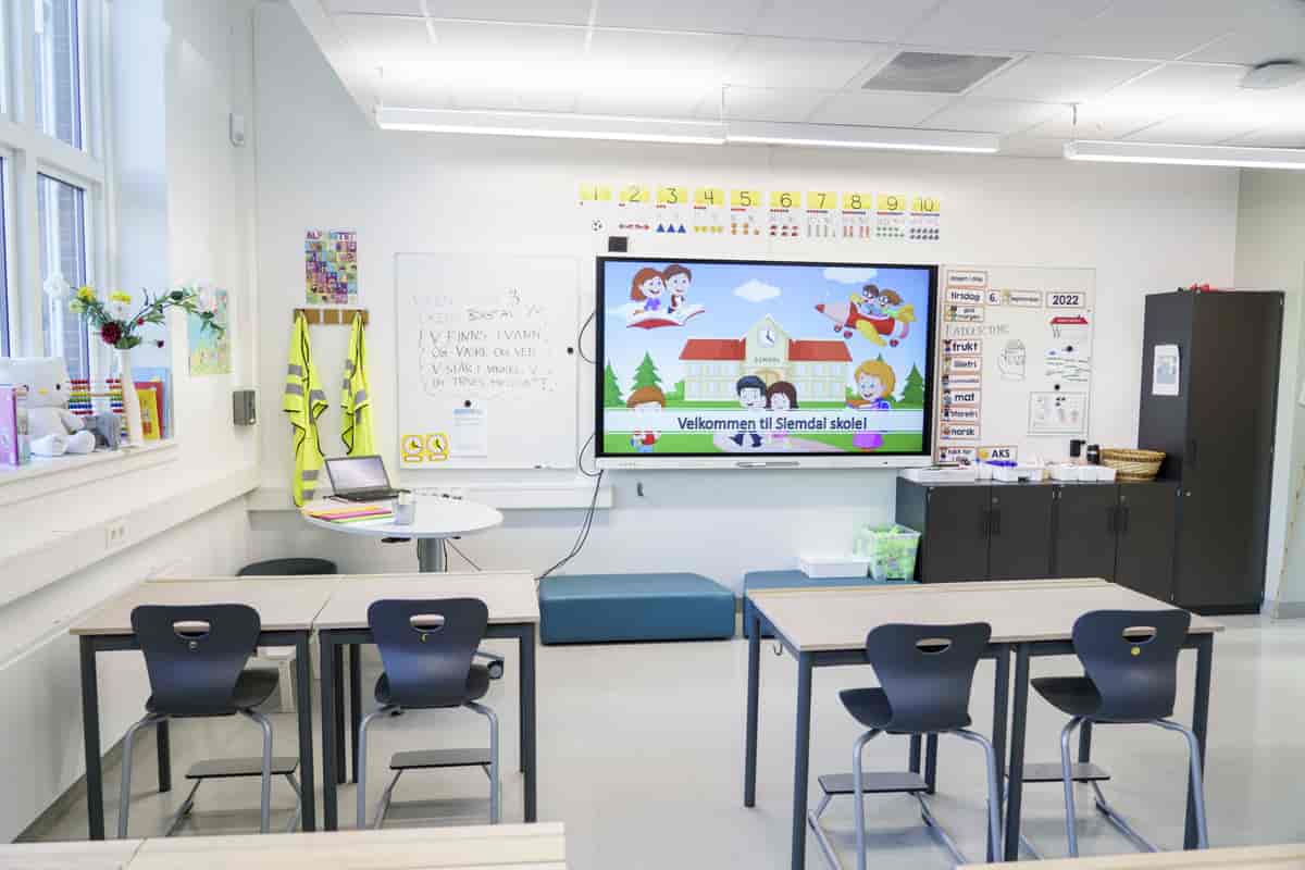 Et tomt klasserom med en interaktiv tavle i bakgrunnen.