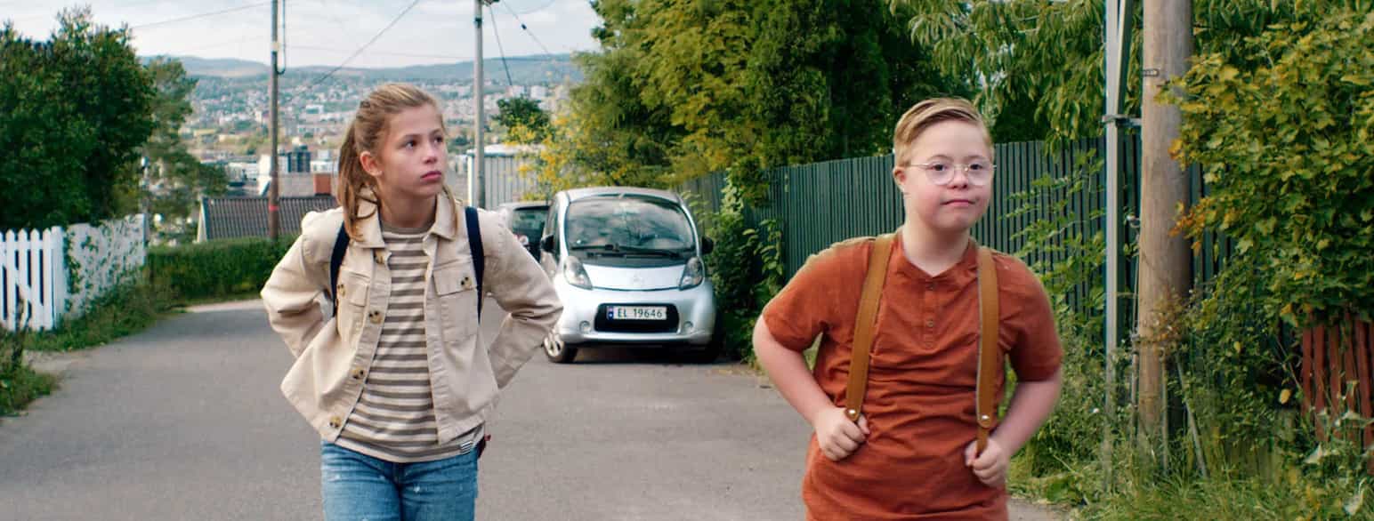 Foto av en gutt og ei jente med skolesekker, på en vei i et boligområde. De går noen meter fra hverandre og snakker ikke sammen.