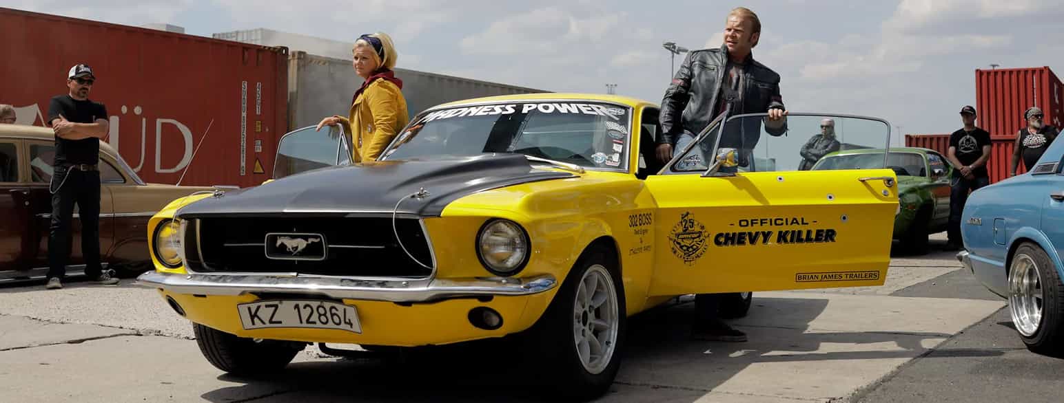Stillbilde fra filmen Børning 3. To personer på vei inn eller ut av en gul og svart bil av merket Mustang. 