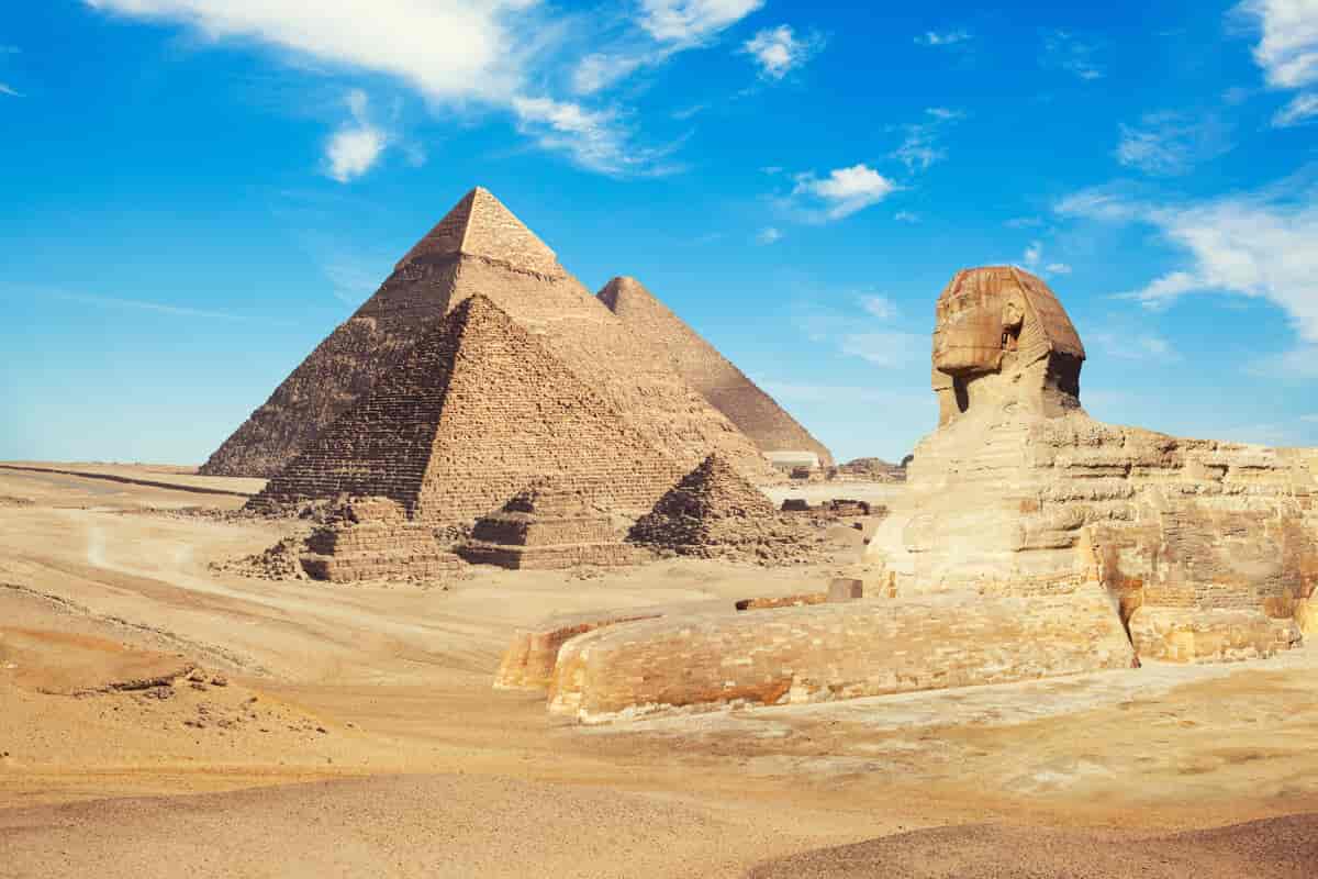 Tre store pyramider og tre små i et ørkenlandskap. I forgrunnen en sfinks, et fabeldyr som er blanding av løve og menneske.