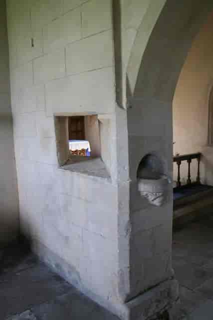 Foto av et hull i en halvvegg i en kirke. Gjennom hullet kan man se deler av et alter. 