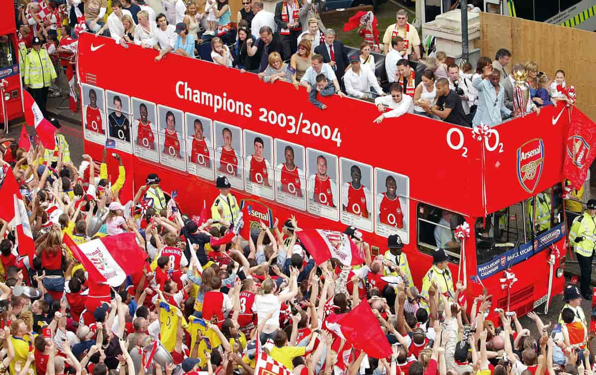 Fotballspillere feirer seriemesterskap på toppen av en åpen buss med supportere på gateplan. 