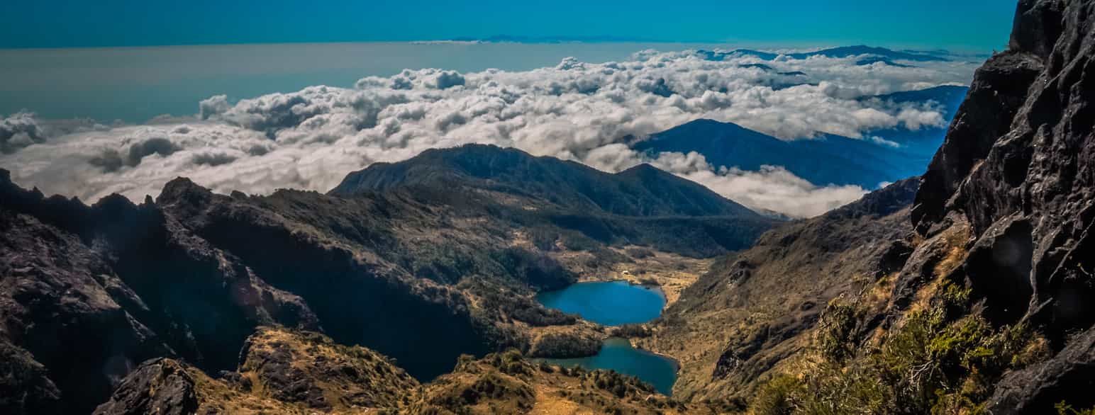 Foto av utsikt over et fjellandskap med innsjø og spisse topper med lave skyer eller tåke.