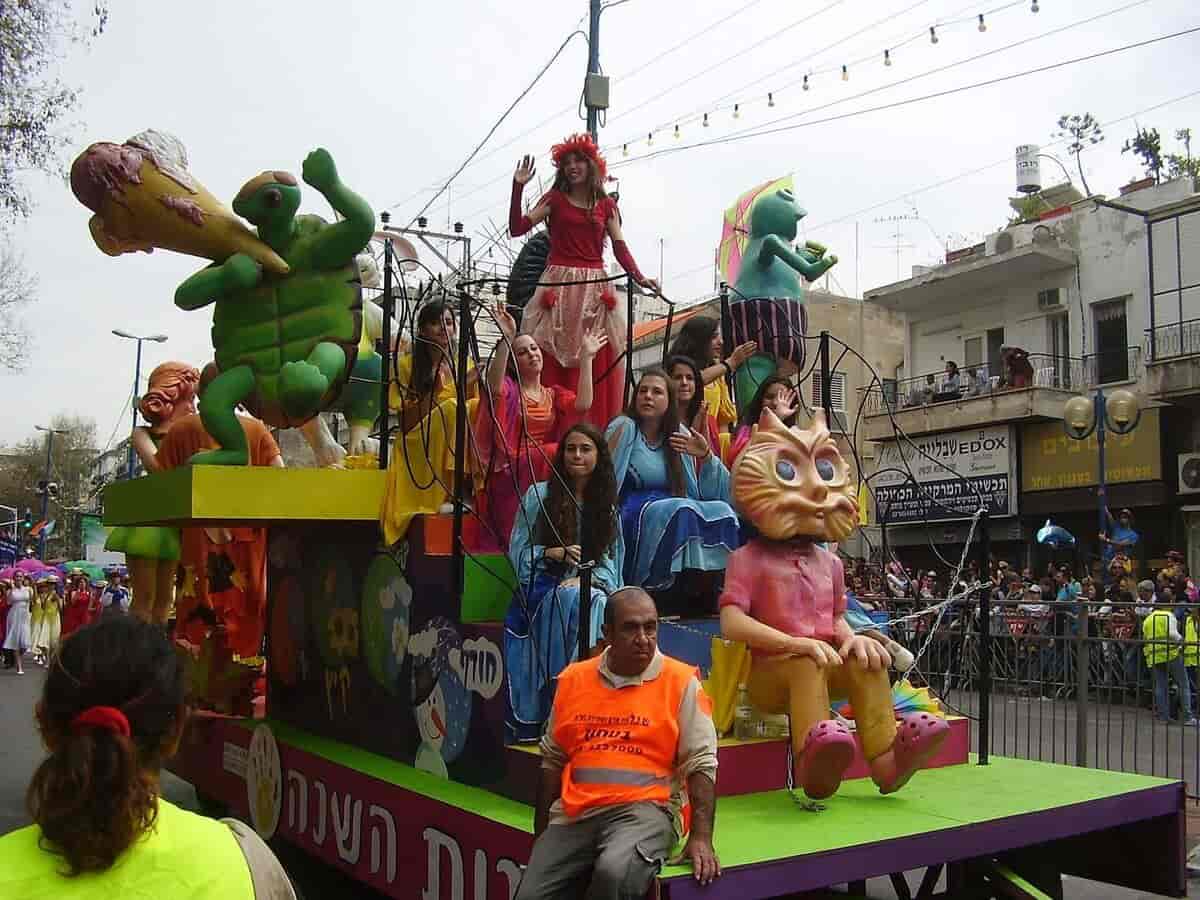 Kvinner i fargerike klær som sitter på et lasteplan på en bil. Det er forskjellige plastfigurer på bilen, en katt, en skilpadde og en dukke.