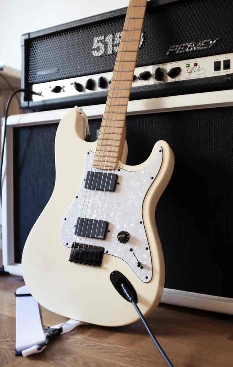 En hvit el-gitar som står foran en forsterker.