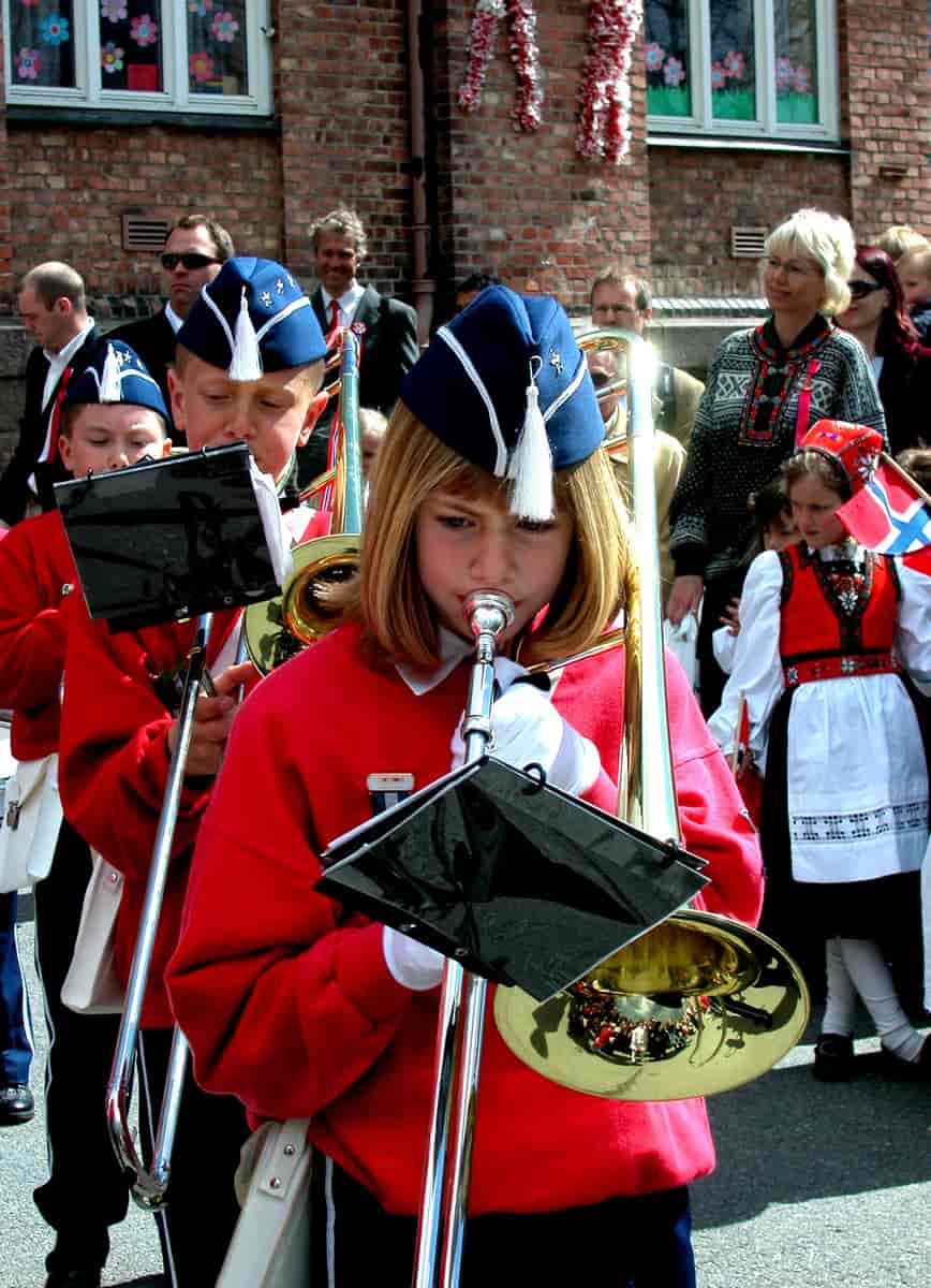 Nærbilde av en gutt og en jente i rød og blå korpsuniform som spiller trombone.