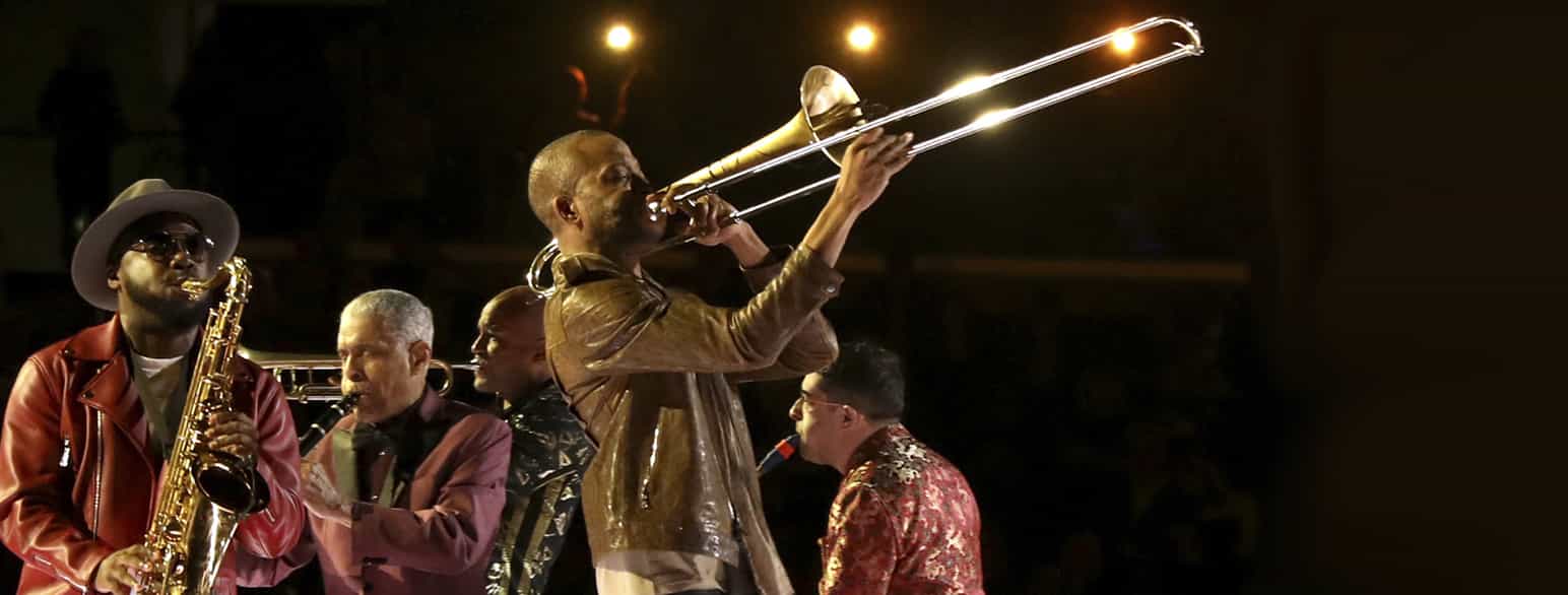 En mann som spiller trombone. Ved siden av ham står det en mann som spiller saxofon.