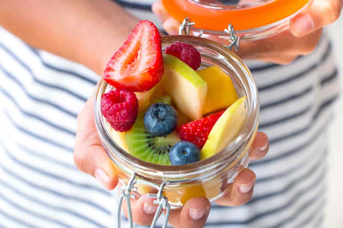 Et syltetøyglass med lokk fylt av bær og frukt i biter