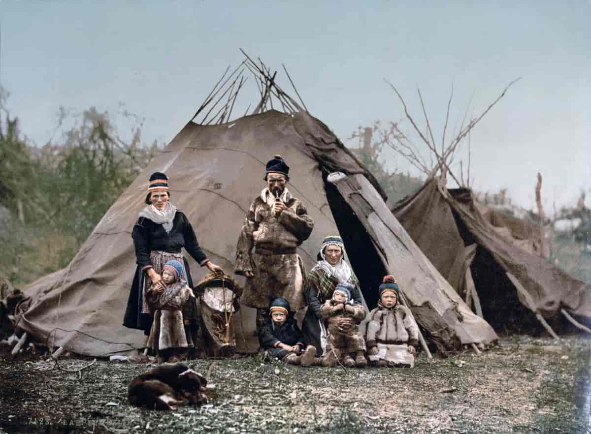 Familie foran en bealljegoahti. Kolorert foto fra cirka 1890-1910.