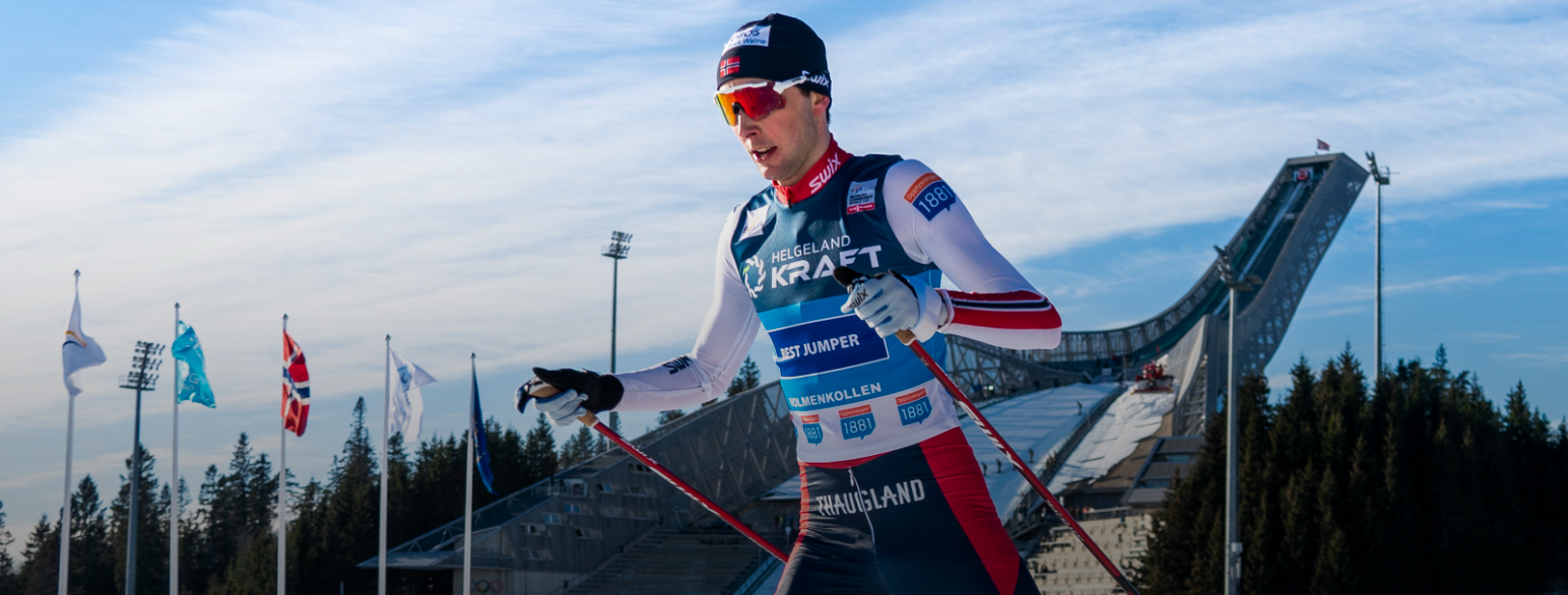Foto av Jarl Magnus Riiber på ski i løypa i Holmenkollen med hoppbakken i bakgrunnen