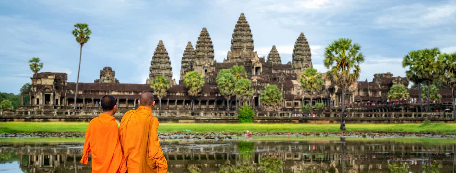 Foto av munker i oransje klær foran tempelruinene i Angkor