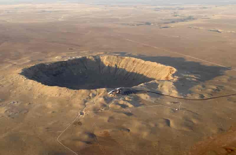 Et stort krater som er et hull i bakken med bratte kanter. Rundt er landskapet gulbrunt og uten planter eller hus.
