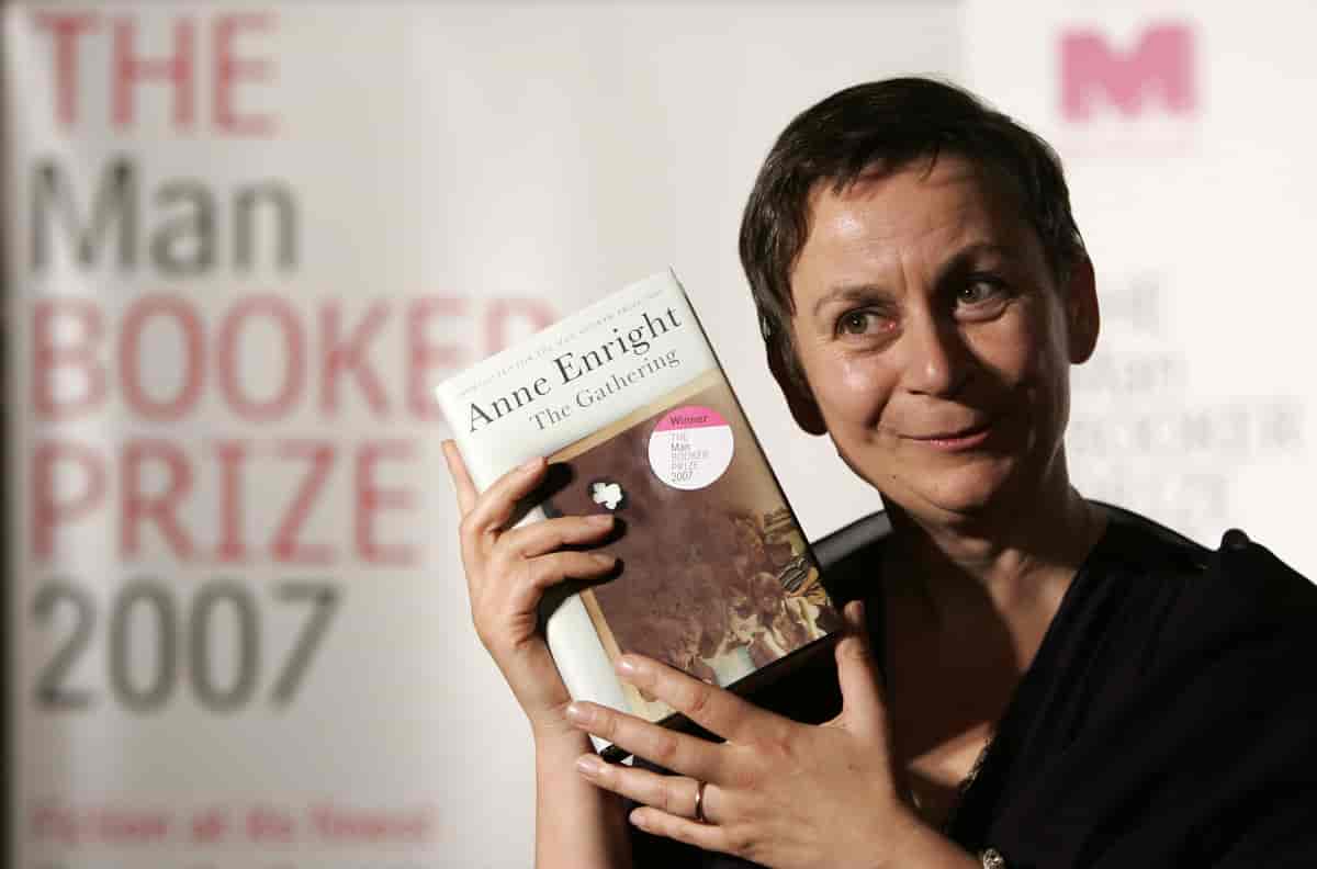 Halvnært foto hvor Anne Enright holder opp boken The Gathering mens hun står foran bannere hvor det står MAN Booker Prize.