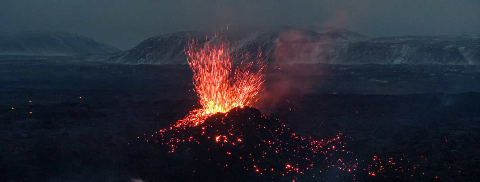 En vulkan som spruter ut rød lava. Bildet er tatt om natten, med svart nattehimmel.