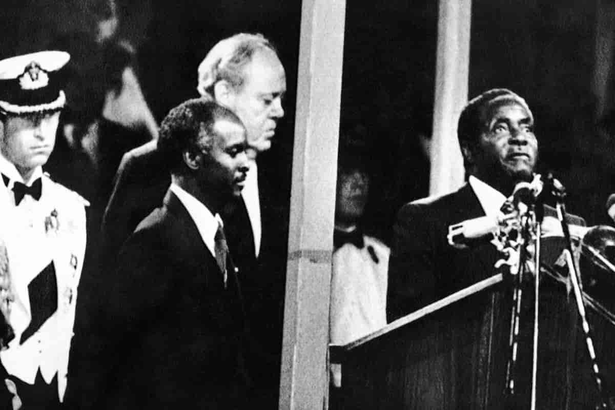Mugabe står på talerstolen med de tre andre mennene bak. 