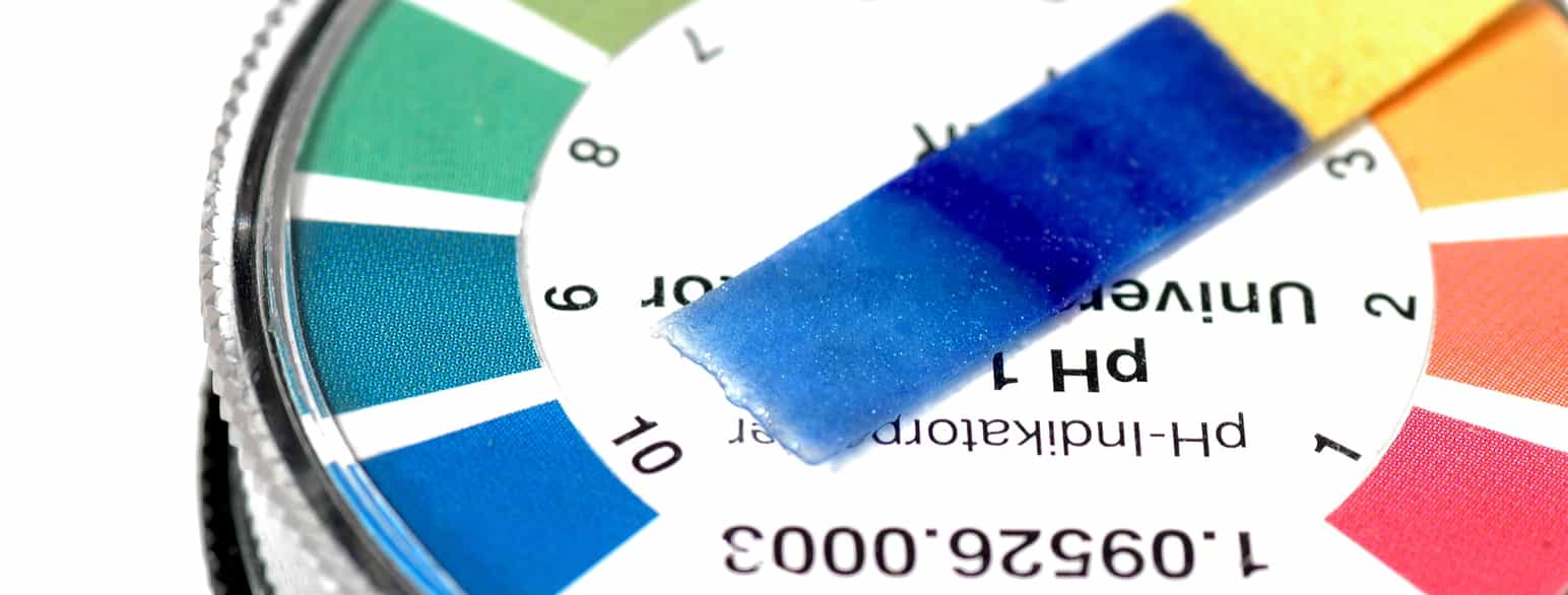 Bildet viser en pH-skala med mest de grønne og blå fargene. Et papir har en blå farge, som viser at det er en basisk væske på den.