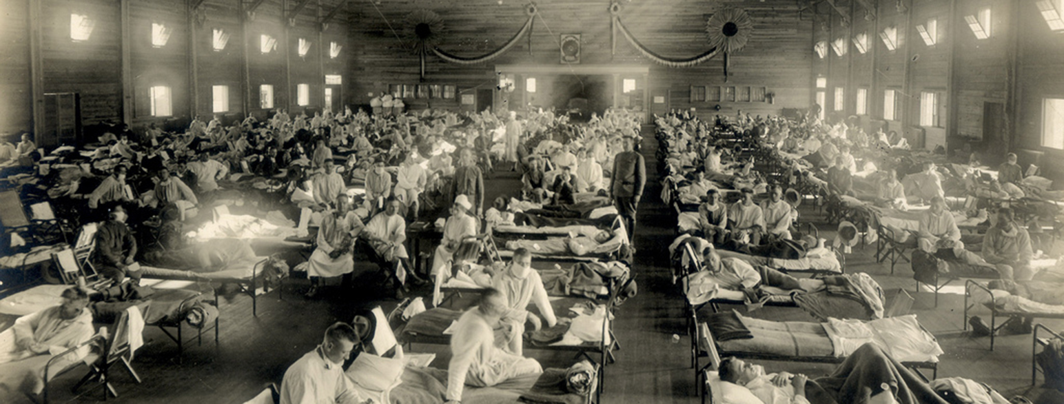 Mange titalls feltsenger er satt opp på rekke og rad i et stort hangarrom. Pasientene ligger eller sitter i sengene. Det er avstand mellom sengene, men rommet er nesten fullt. Leger og sykepleiere i hvit uniform ser til pasientene. Flere helsepersonell har på seg munnbind.