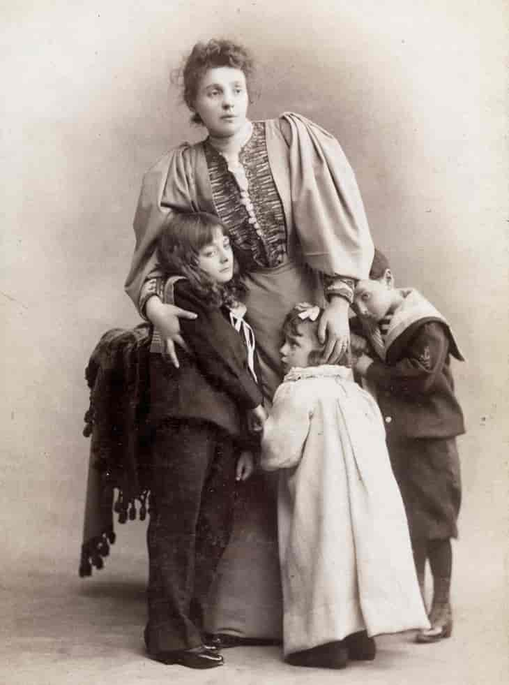 et svart/hvitt bilde av en kvinne som holder rundt tre små barn.