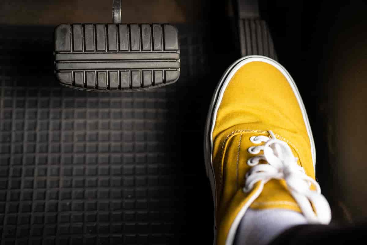En fot med en gul sko som tråkker på en gasspedal i en bil.