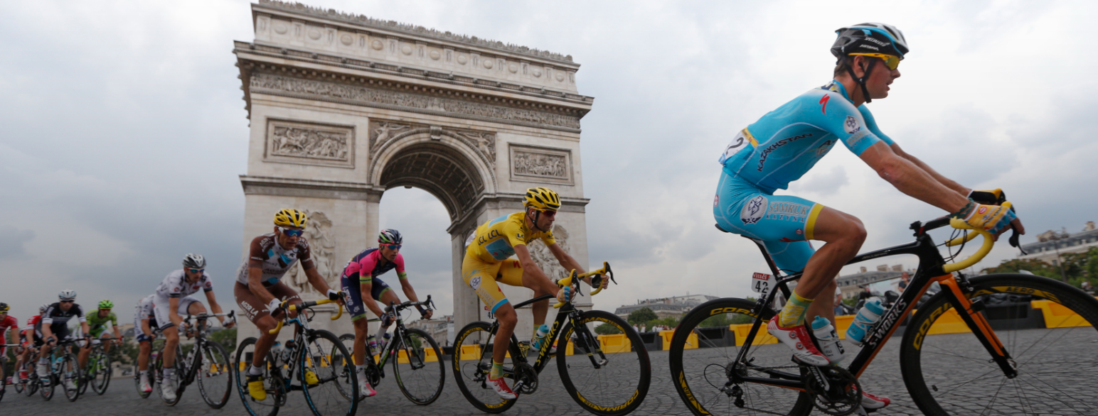 Sykkelryttere sykler på rekke foran Triumfbuen i Paris