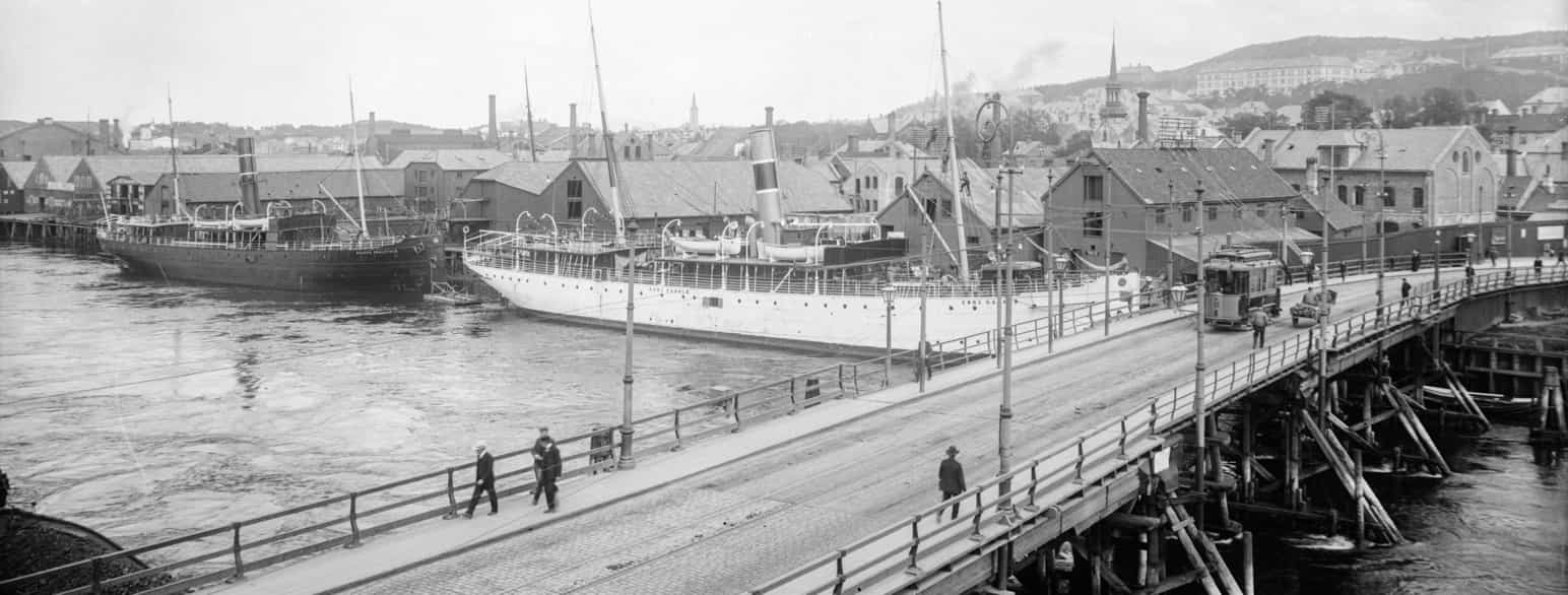 Bakke bru i Trondheim, ca 1910. Trafikken består av trikk, hest og karjol, og noen personer. To skip ligger fortøyd ved Nordre Verft, D/S Kong Harald og D/S Håkon Adalstein.