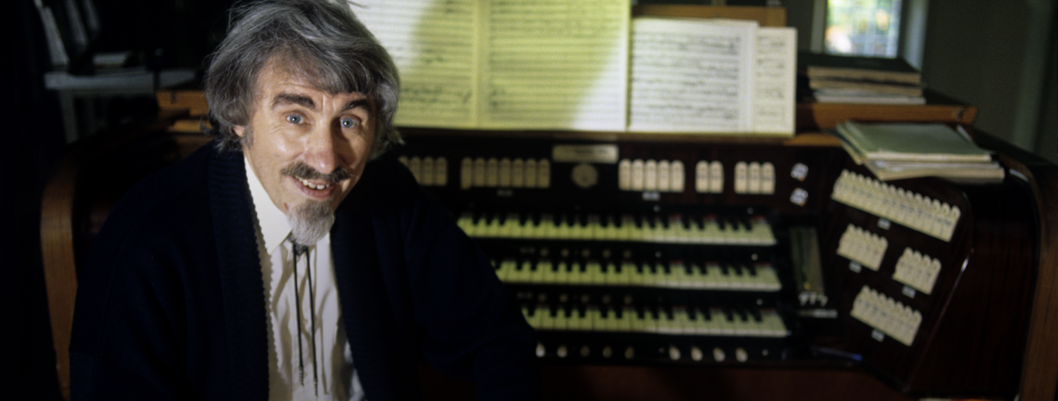 Foto av komponisten Egil Hovland. Han sitter foran et orgel. Det ligger flere noter og partiturer rundt ham. 