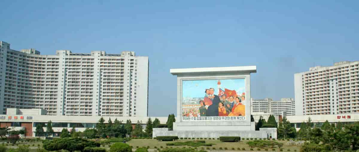 Tre store blokker i Pyongyang i Nord-Korea. En av blokkene har et stort veggmaleri av Kim Il Sung og koreanere.