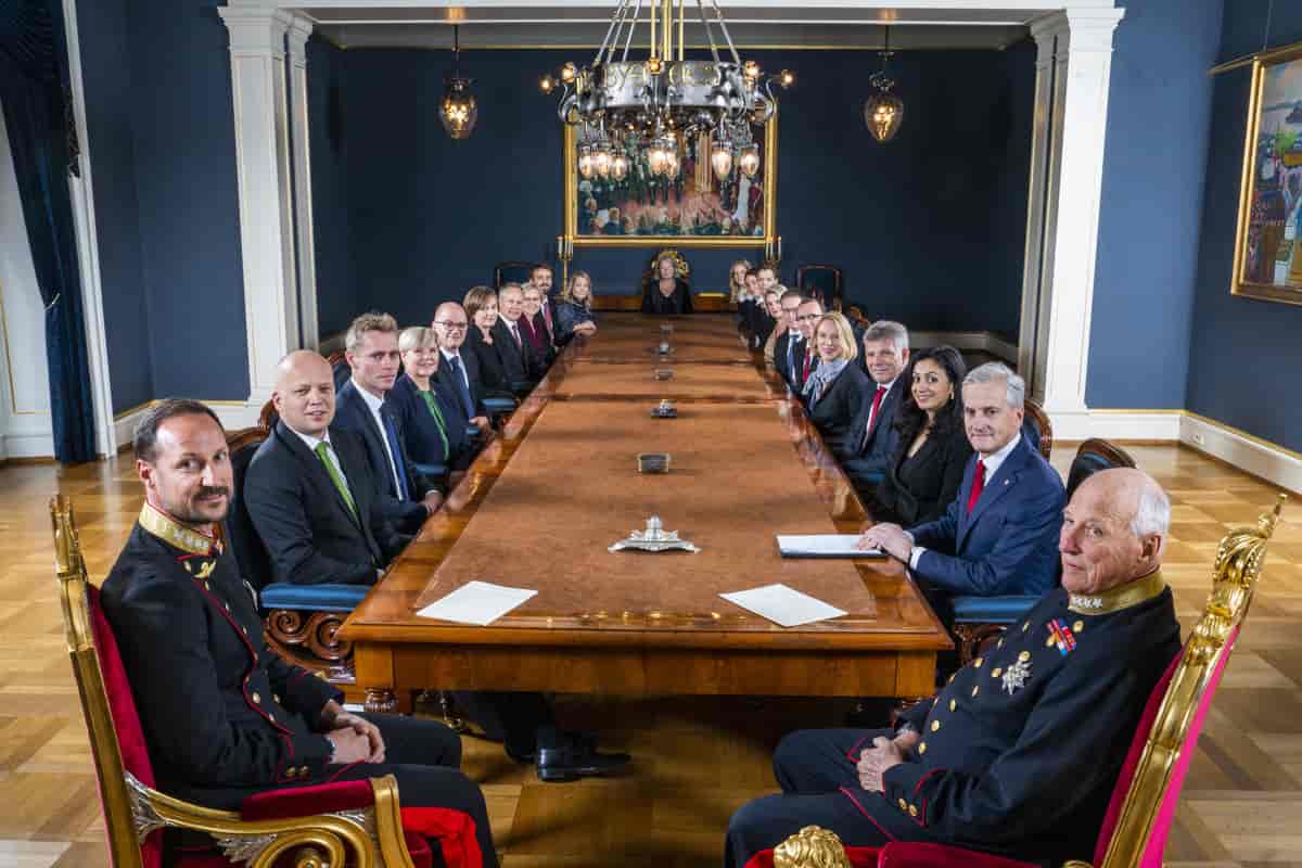 Foto fra statsråd med kronprins Haakon og kong Harald nærmest kamera. Nedover på hver side av et langt langbord sitter regjeringsmedlemmene. 