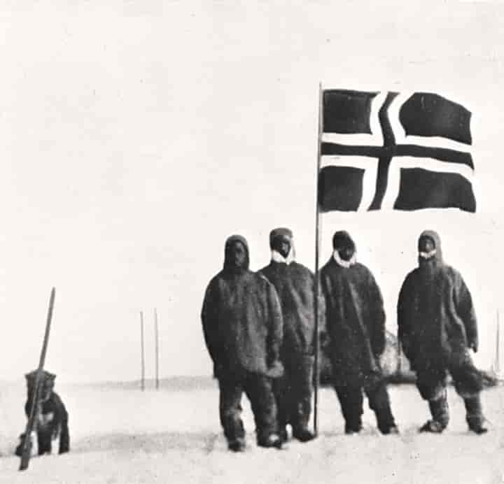 Fire menn står foran et norsk flagg på et snødekt landskap.