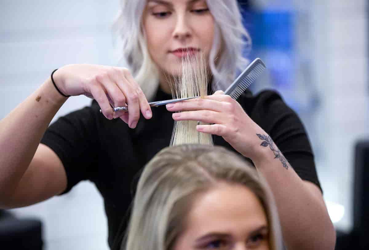 En frisør holder håret til en kvinne mellom fingrene og klipper det med saks