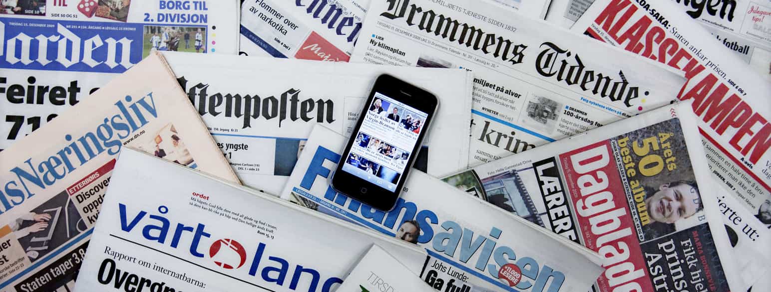 Flere ulike norske aviser som ligger oppå hverandre. På toppen ligger en smart-telefon med forsiden til en avis.