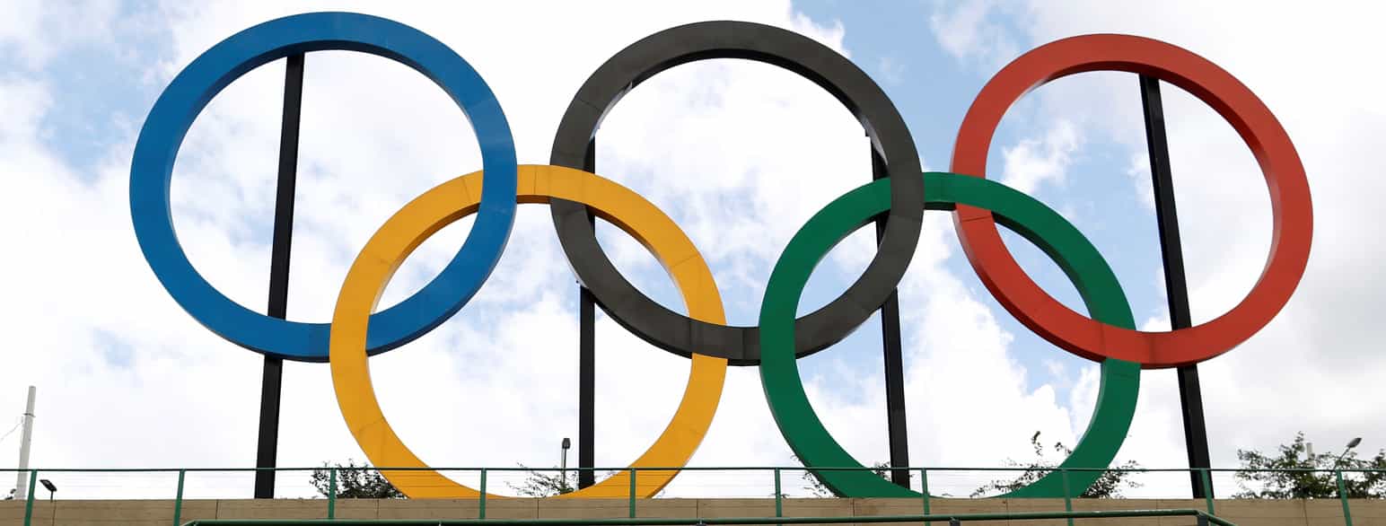Foto av OL-ringene som en slags skulptur. Ringene overlapper og går i hverandre, tre oppe, og to nede. Fargene på ringene er øverst fra venstre blå, svart, rød, nederst fra venstre gul og grønn. 