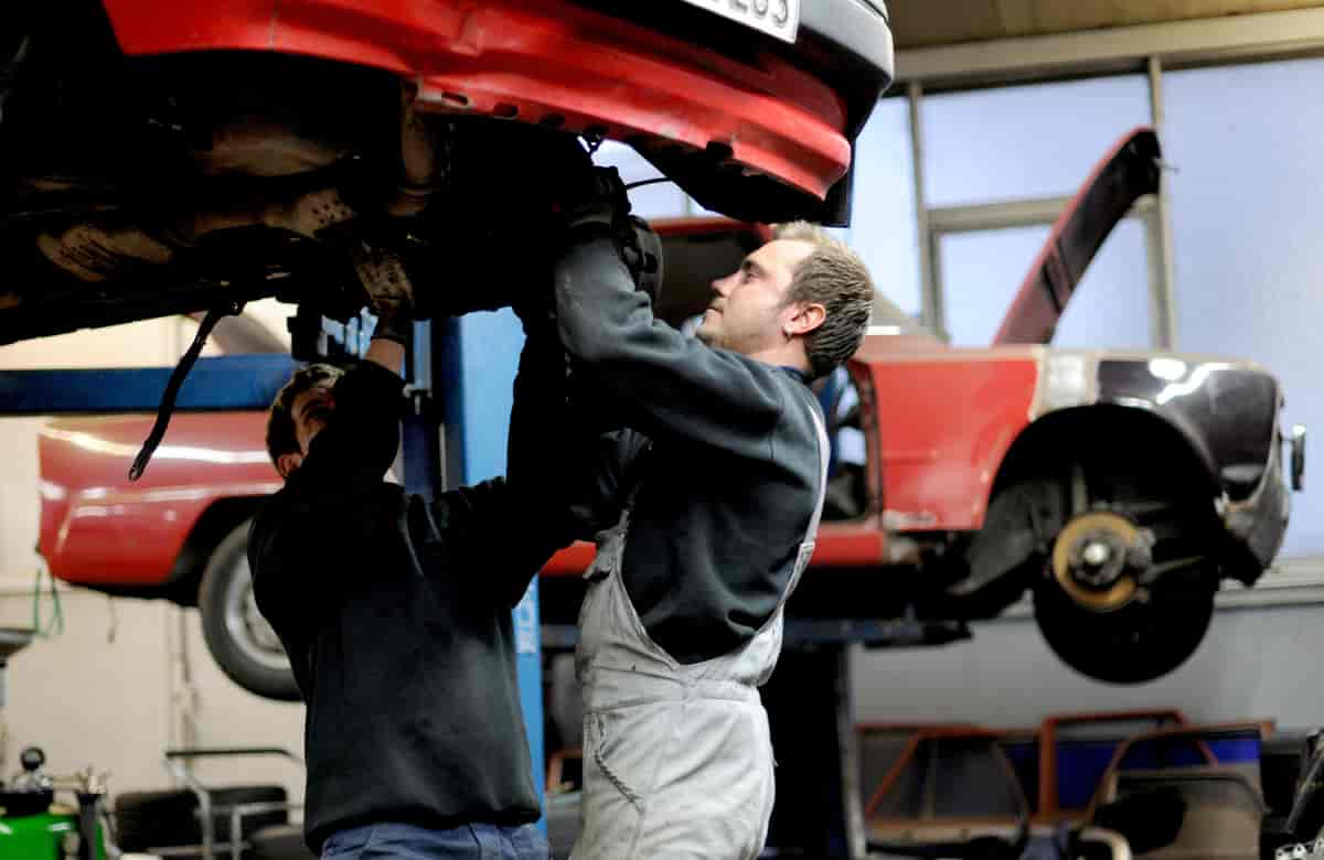 Foto av to bilmekanikere som står under en bil og reparerer den.
