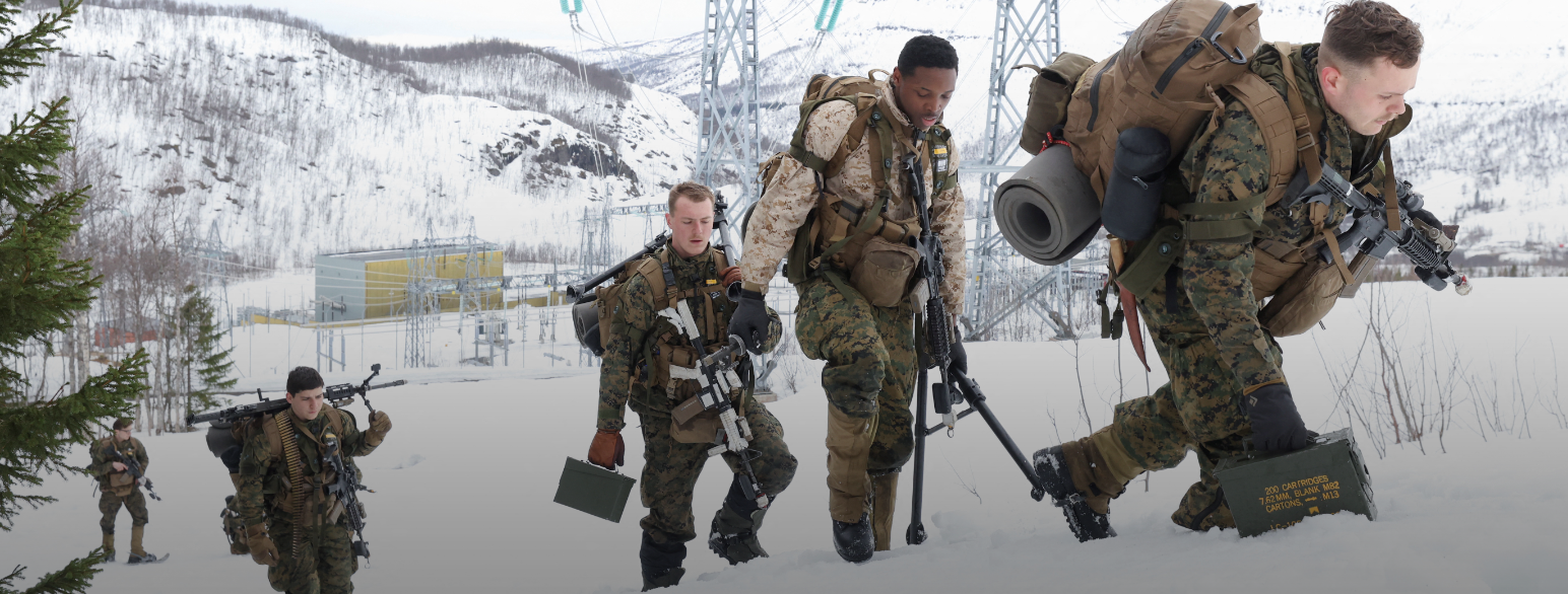 soldater i uniform forserer en åsrygg i snøen under en militærøvelse. De bærer med seg våpen.
